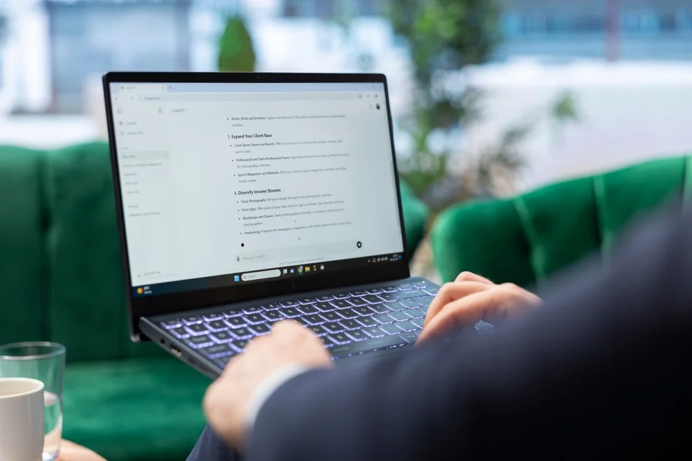 Person typing on a laptop displaying a ChatGPT document interface while sitting in a green velvet armchair.